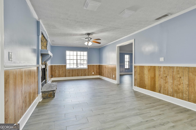 unfurnished living room featuring a wainscoted wall, ceiling fan, visible vents, and a textured ceiling