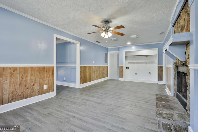 unfurnished living room with light wood finished floors, a fireplace with raised hearth, a textured ceiling, and wainscoting