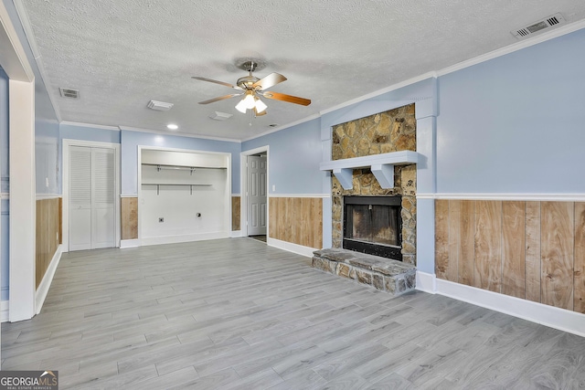 unfurnished living room featuring a textured ceiling, ceiling fan, a fireplace, visible vents, and wainscoting