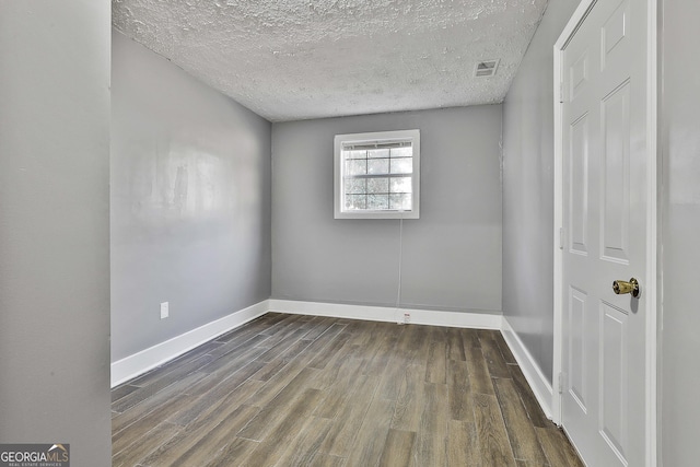 empty room featuring dark wood-style floors, a textured ceiling, visible vents, and baseboards