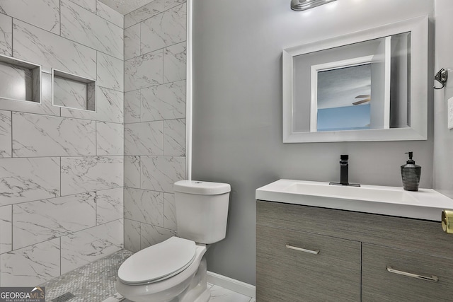 bathroom featuring marble finish floor, toilet, vanity, tiled shower, and baseboards