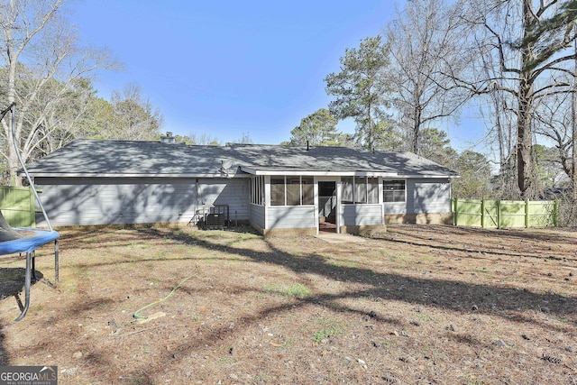 back of property with a sunroom, a trampoline, and fence