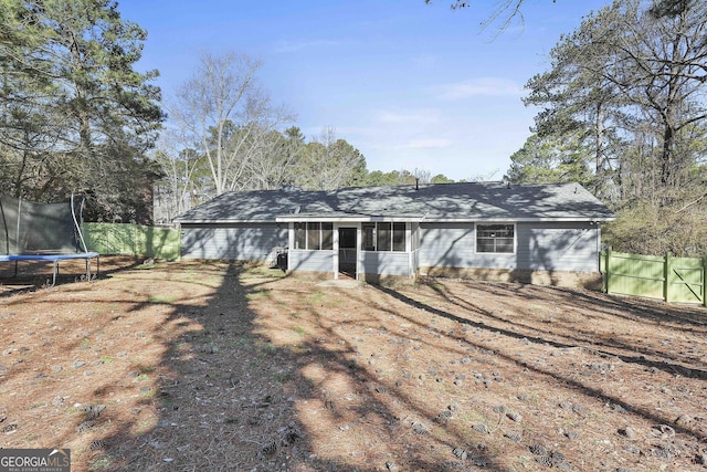 rear view of house featuring a trampoline, fence, and a sunroom