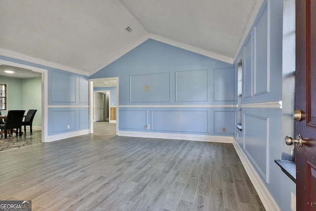 living area with vaulted ceiling, visible vents, a decorative wall, and light wood finished floors