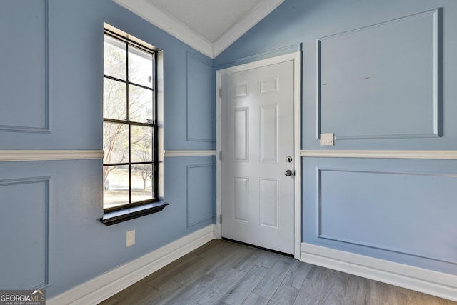 doorway featuring vaulted ceiling, crown molding, wood finished floors, and a decorative wall