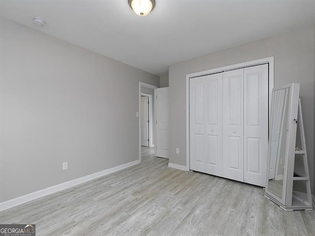 unfurnished bedroom featuring light wood finished floors, a closet, and baseboards