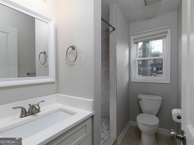 bathroom featuring vanity, a tile shower, toilet, and baseboards