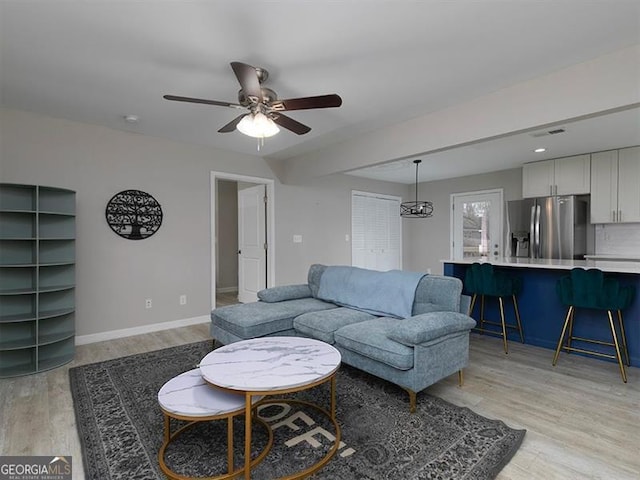 living area with a ceiling fan, light wood-type flooring, visible vents, and baseboards