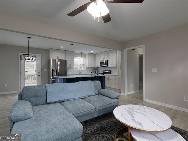 living room featuring ceiling fan, light wood-style flooring, and baseboards