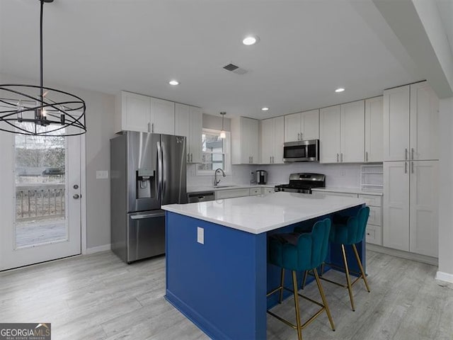 kitchen with light wood finished floors, visible vents, a kitchen island, appliances with stainless steel finishes, and white cabinetry