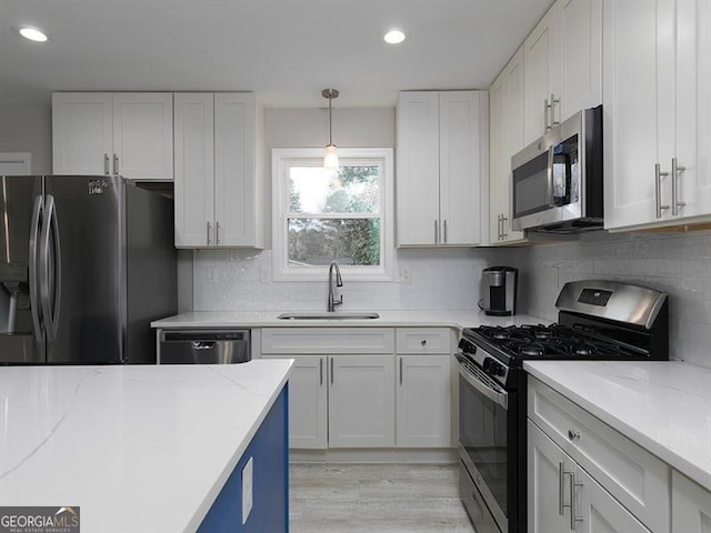 kitchen with light stone counters, stainless steel appliances, a sink, white cabinets, and tasteful backsplash