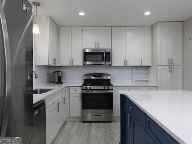 kitchen with white cabinets, blue cabinetry, stainless steel appliances, and a sink