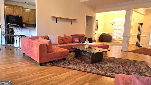 living room featuring light wood-style floors, a chandelier, crown molding, and ornate columns