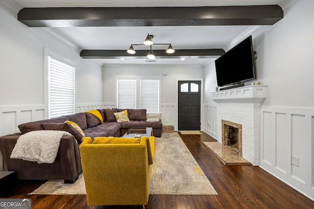 living room featuring beamed ceiling, a decorative wall, dark wood-style floors, and wainscoting