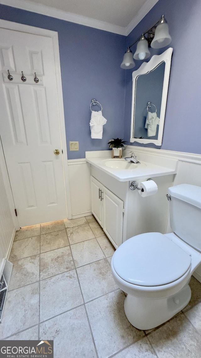 half bathroom with ornamental molding, wainscoting, vanity, and toilet