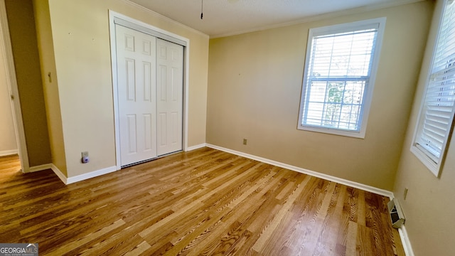 unfurnished bedroom with a closet, crown molding, baseboards, and wood finished floors