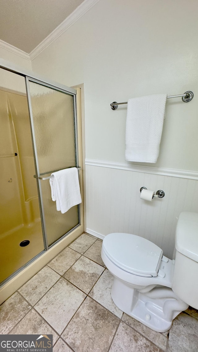 bathroom featuring ornamental molding, a wainscoted wall, a shower stall, and toilet