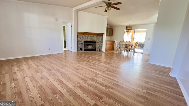 unfurnished living room with light wood finished floors, baseboards, a ceiling fan, vaulted ceiling, and a stone fireplace