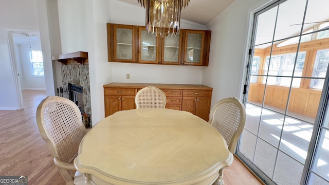 dining space featuring light wood-type flooring, baseboards, ornamental molding, and a stone fireplace