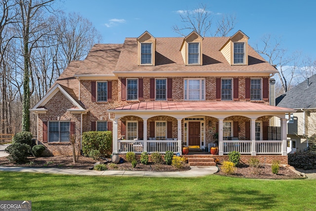 view of front facade featuring roof with shingles, a front lawn, a porch, and brick siding