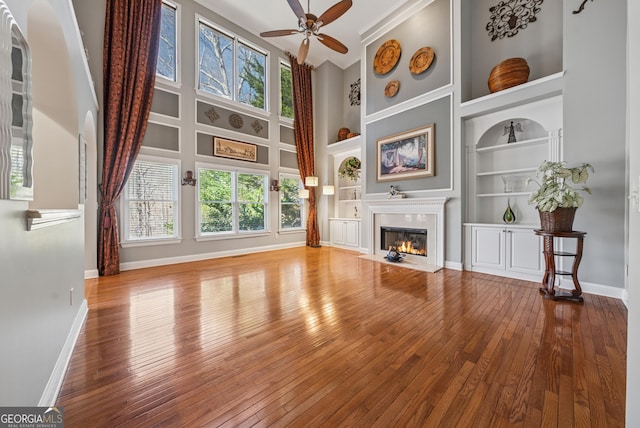 living room featuring a high ceiling, a fireplace with flush hearth, baseboards, built in features, and wood-type flooring