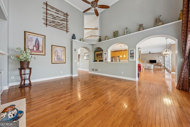 unfurnished living room with ceiling fan with notable chandelier, arched walkways, and hardwood / wood-style flooring