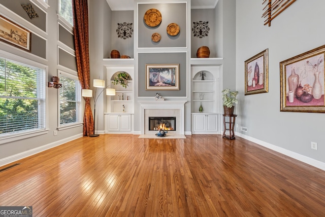 unfurnished living room featuring built in shelves, a fireplace with flush hearth, hardwood / wood-style floors, and baseboards