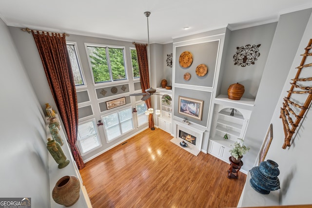 sitting room with a lit fireplace, built in shelves, ornamental molding, and light wood-style flooring