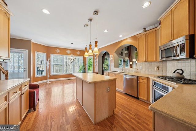 kitchen featuring stainless steel appliances, light countertops, ornamental molding, decorative backsplash, and a center island