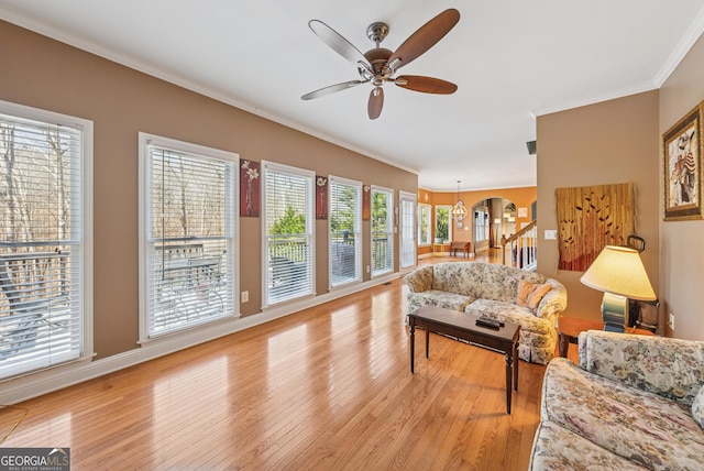 living room featuring ceiling fan, arched walkways, stairs, ornamental molding, and light wood finished floors