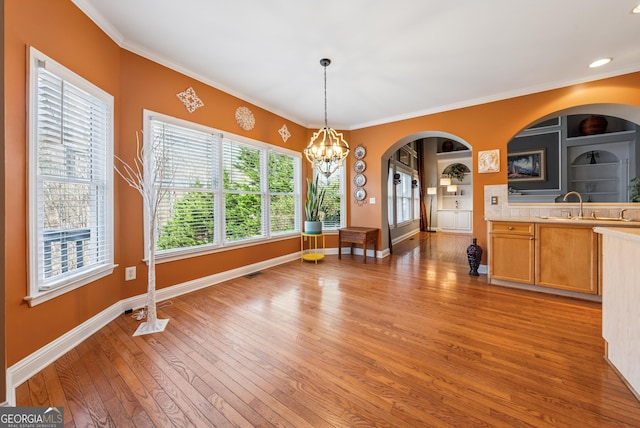 dining room featuring baseboards, built in features, arched walkways, an inviting chandelier, and light wood-style floors