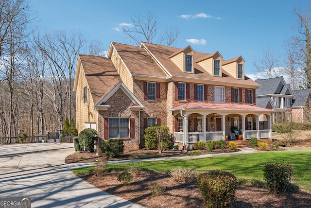 view of front of home with covered porch, driveway, brick siding, and a front lawn