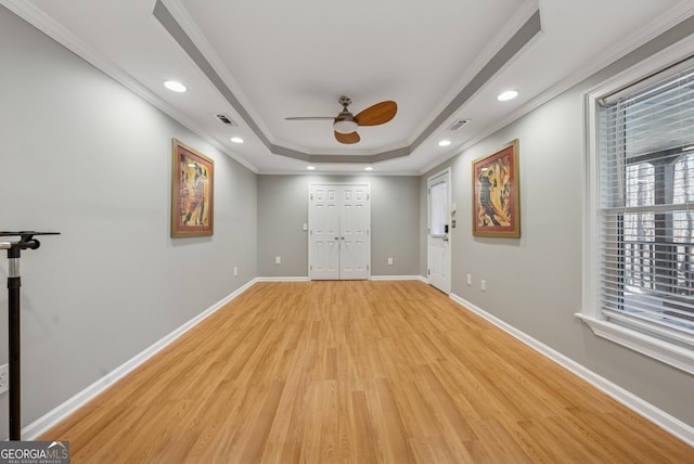 interior space with visible vents, baseboards, a raised ceiling, crown molding, and light wood-style floors