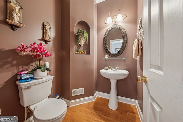 half bathroom featuring toilet, baseboards, visible vents, and wood finished floors