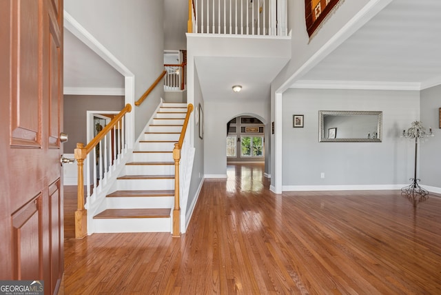 entrance foyer with arched walkways, a high ceiling, wood finished floors, baseboards, and crown molding