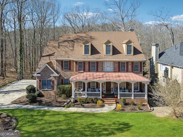 view of front of property featuring driveway, a shingled roof, covered porch, a front lawn, and brick siding