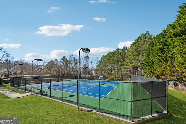 view of tennis court with a yard and fence