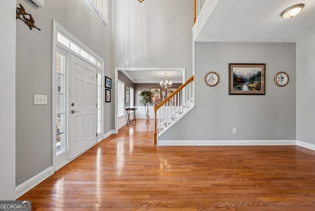 foyer featuring hardwood / wood-style flooring, a high ceiling, baseboards, stairs, and an inviting chandelier