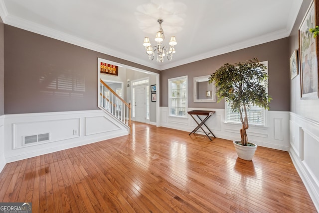 foyer entrance featuring visible vents, ornamental molding, stairway, hardwood / wood-style floors, and an inviting chandelier