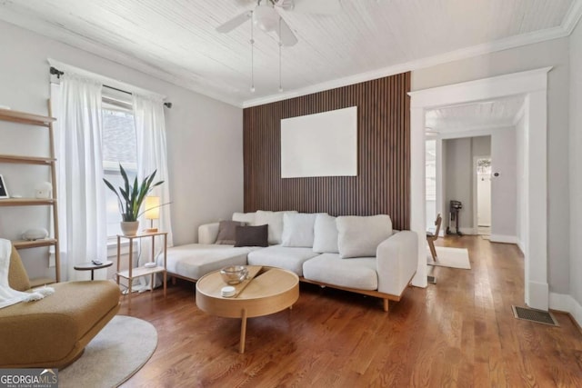 living room with ceiling fan, wood finished floors, visible vents, baseboards, and crown molding