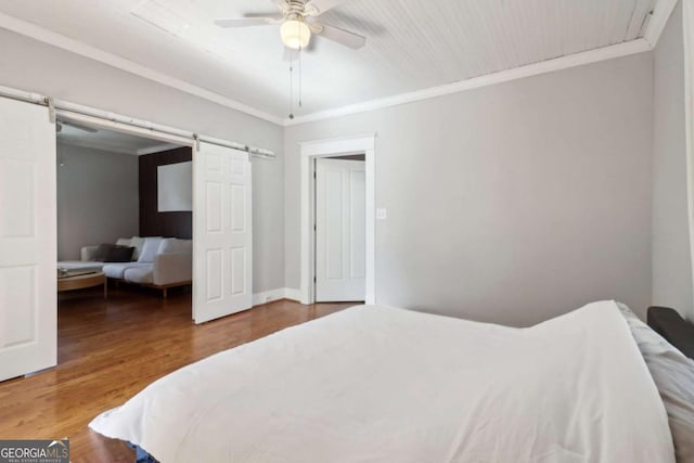 bedroom with wood finished floors, crown molding, and a barn door