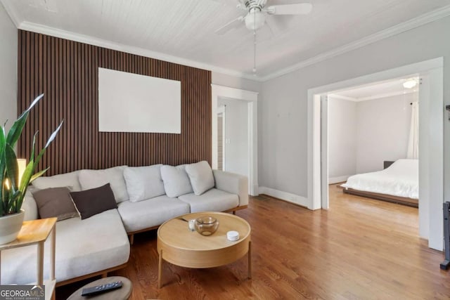 living area with baseboards, wood finished floors, a ceiling fan, and crown molding