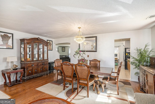 1134 Saint Phillips Ct, Locust Grove, GA 30248 - dining space featuring an inviting chandelier, visible vents, a textured ceiling, and wood finished floors