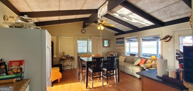 dining space with light wood-style floors, vaulted ceiling with beams, and a ceiling fan