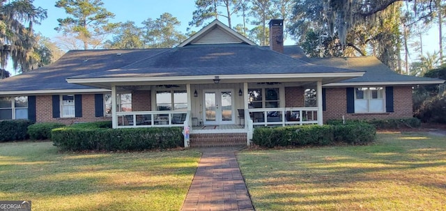 view of front facade featuring french doors, brick siding, a chimney, a porch, and a front yard