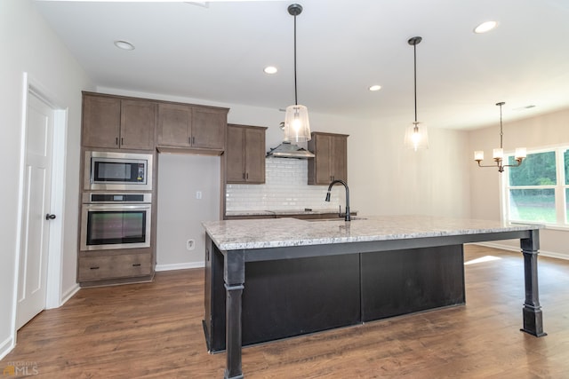 kitchen with stainless steel appliances, an island with sink, a sink, and decorative light fixtures