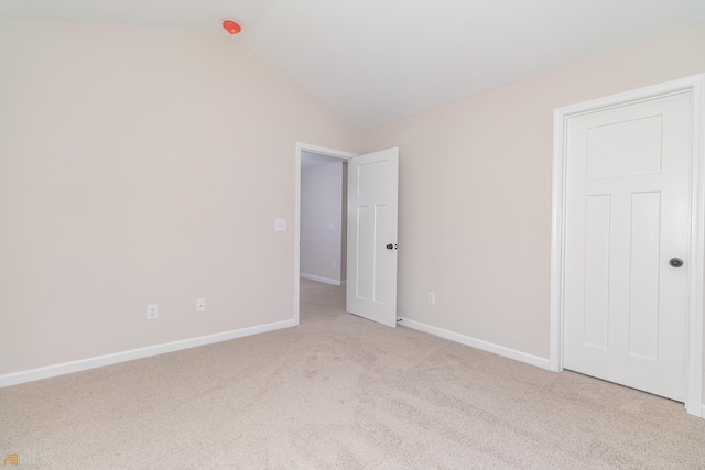 unfurnished bedroom with vaulted ceiling, baseboards, and light colored carpet