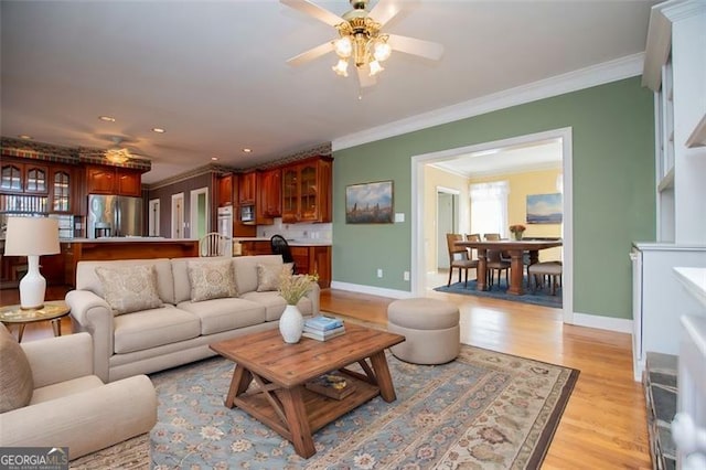 living area featuring ornamental molding, light wood-type flooring, a ceiling fan, and baseboards