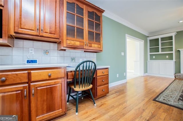 office space featuring built in desk, crown molding, light wood-style flooring, and baseboards