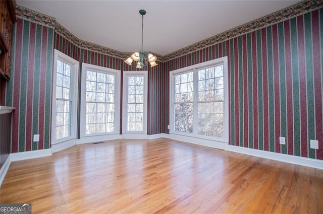 unfurnished dining area featuring a notable chandelier, wood finished floors, a healthy amount of sunlight, baseboards, and wallpapered walls